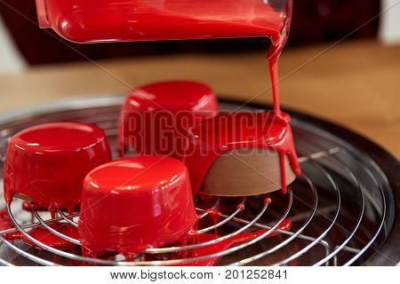 cooking, baking and food concept - jug pouring glaze to chocolate cakes on tray with grid at pastry shop