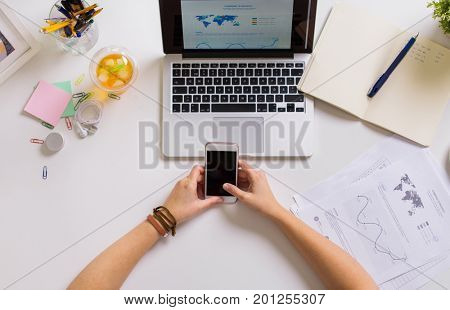 business, people and technology concept - hands with smartphone and laptop at office table