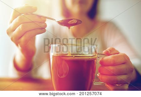 healthy food, eating and ethnoscience concept - close up of woman adding honey to tea cup with lemon