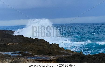 Blue ocean crashing on the black rocky shore