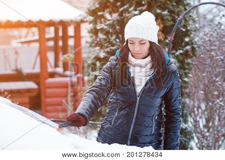 Young attractive woman in the winter clothes removes snow from car with snow brush.Toned.