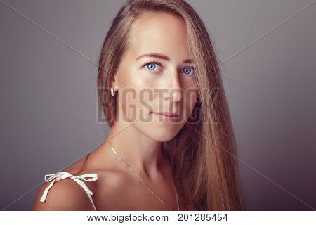 Portrait of calm pensive Caucasian blonde young beautiful girl woman model with long hair and blue eyes in white dress. Slav european model posing in studio on plain light background.