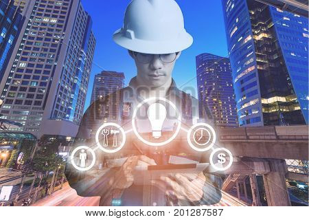 Double exposure of Engineer or Technician man with business industrial tool icons while using tablet with light of night commercial building for constrution business concept.