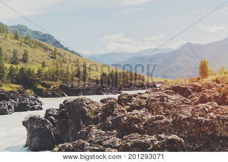Scenery of the most narrow place of Katun river in Altai mountains with distant meadows and hills in haze and mossy huge stones in foreground summer sunny day Kuyus district Russia