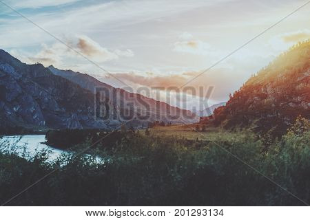 Scenery of stunning sunset on Altai mountains near Katun river in Kuyus district Russia: bend of river partly closed by grass in foreground mountain range lit by evening sun meadows and trees