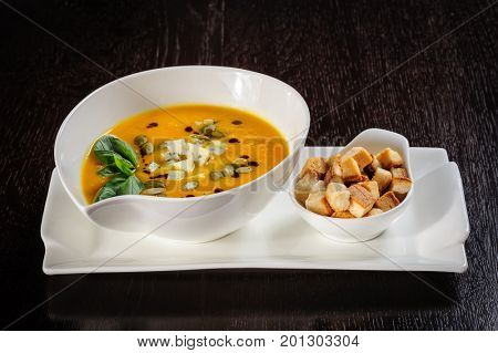 Pumpkin soup with cream and pumpkin seeds on dark wooden background. Copy space.