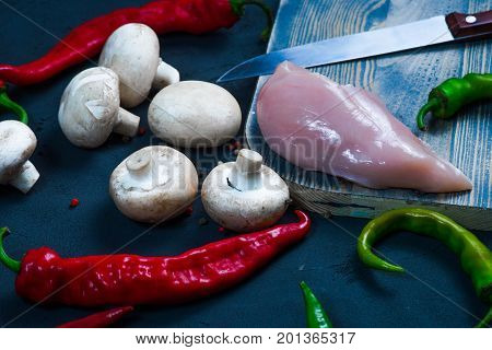 raw chicken wings with herbs in a transparent bowl Cauliflower with tomatoes and herbs and hot peppers with mushrooms on wooden background top view close up.