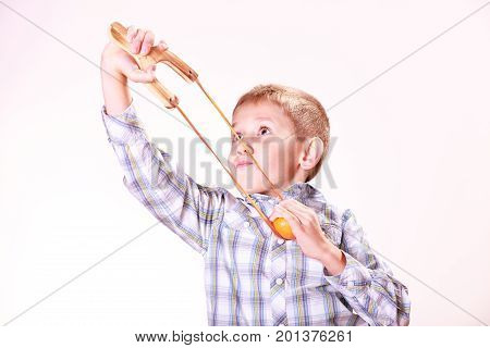 Nature and free time prankster little boy. Child have fun with wooden sling shot and fruit aim mandarine.
