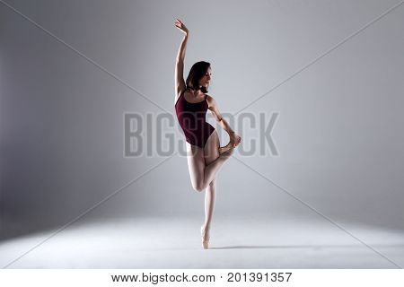 Slim ballerina is dancing in the white studio in the contrast light