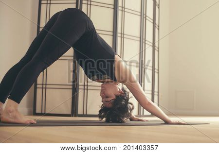 A young woman performing yoga-asanas in the hall. Artha mukha svanasana.