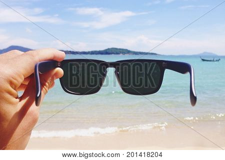 Man's Hand Holding Hipster Style Sunglasses on the Rawai Beach. Travel Lyfestyle Carefree Tourism Concept. Phuket, Thailand