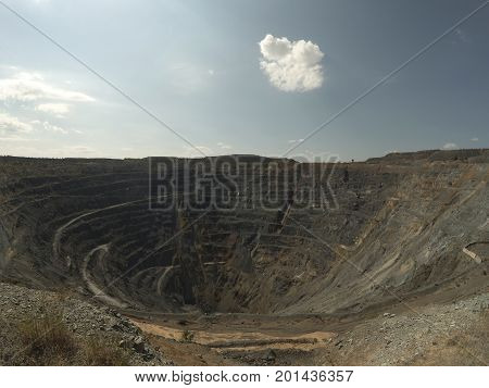 Big Abandoned opencast mining quarry against cloud sky.