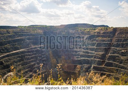 Big Abandoned opencast mining quarry against cloud sky.
