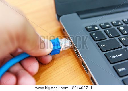 Human hand plugging in a LAN cords into the personal laptop computer Close up