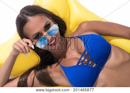 Sexy tanned brunette in nice blue bicini and color sunglasses smiling and enjoying her summer weekend sunny shot