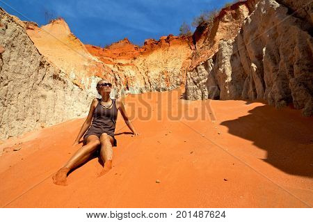 Young attractive woman in dress and sunglasses sitting in sand dunes and looking at sky