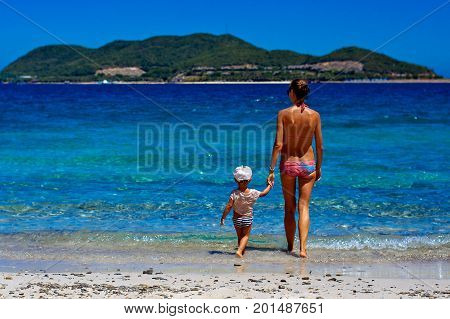 Happy mom and her adorable little daughter during summer vacation on the tropical beach