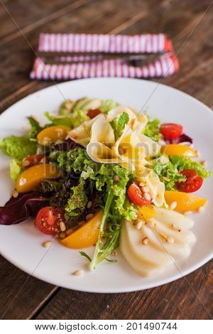 Green salad with cheese and fruits on plate. Lettuce, fresh vegetables decorated pine nuts, avocado, pearch and pear, serving in restaurant
