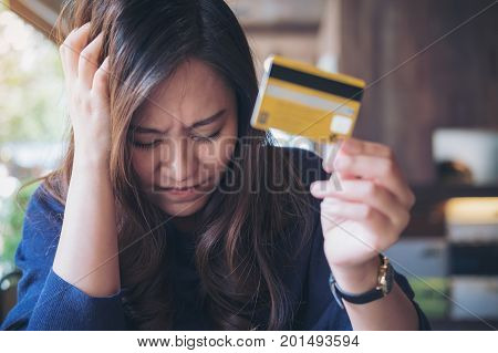 Close up image of an Asian woman close her eyes while holding credit card with feeling stressed and broke