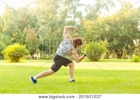 Workout in summer morning. Muscules redhead athlete posing at camera. Outdoor