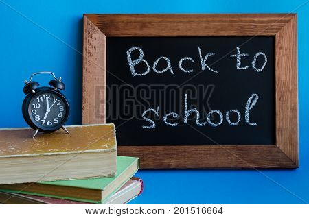 Back to school concept. School supplies on blue background. Frase Back to school written on blackboard with old books and clock.