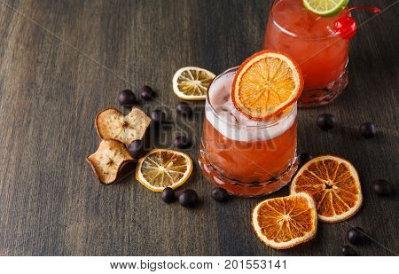 Cocktail on rustic wood background. Cold citrus alcohol beverage with tequila, blood orange juice and ginger beer, served with ice, citrons and chocolate snacks, copy space