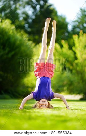 Happy Young Child Playing Head Over Heels On Green Grass In Spring Park