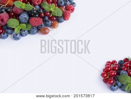 Various fresh summer berries on white background. Ripe raspberries strawberries blueberries gooseberries blackberries blackcurrants and red currants mint. Berries at border of image with copy space for text. Background berries. Top view.