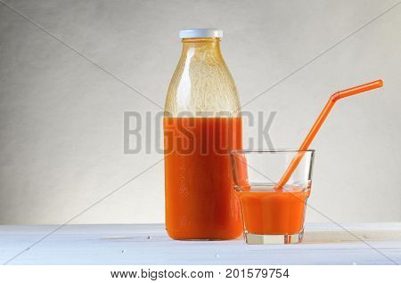 A bottle of carrot juice and a glass of carrot juice with a straw on white wood table. Still life of a healthy eating concept
