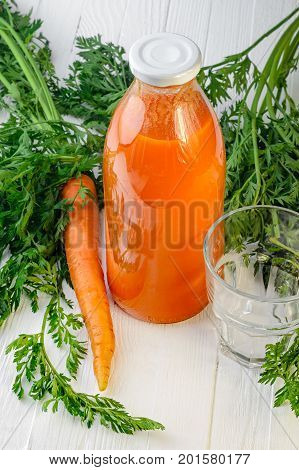 A bottle of carrot juice with empty glass and some fresh carrots on white wood table. Still life of a healthy eating concept
