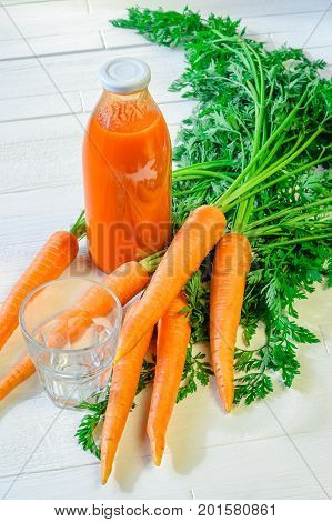 A bottle of carrot juice with empty glass and some fresh carrots on white wood table. Still life of a healthy eating concept