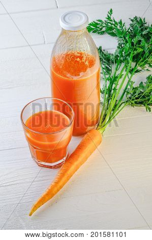 A bottle of carrot juice with with a stuffed glass and one fresh carrots on white wood table. Still life of a healthy eating concept