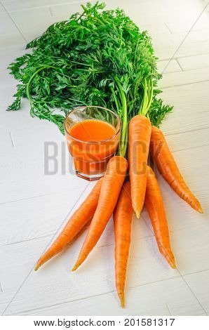 Glass of carrot juice with a bunch of fresh carrots on a white wooden table top view. Still life of a healthy eating concept