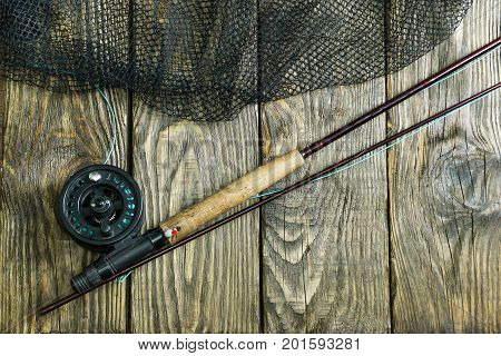 Fly fishing rod ,flie and a landing net on the old wooden table. All ready for fishing.