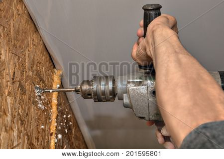 Builder drills in wooden wall communication hole working hand close-up.
