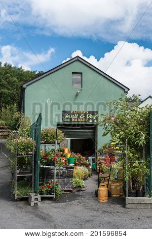 Clifden Ireland - August 4 2017: The green facade and display garden of the small business local Fruit and Vegetable market. Under blue and white sky with plenty of flower colors and plant greens.