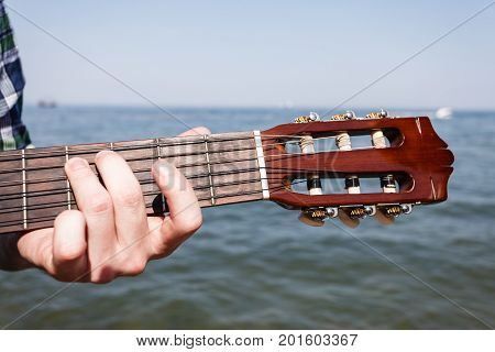 Music sound passion talent relax outdoor leisure concept. Guitarist playing next to sea. Young man with guitar sitting on coast playing instrument.
