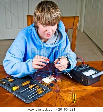 Teen boy uses an ohmmeter to measure resistance across a circuit for a science project.