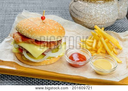 Cheese burger with bakon garnished with sauces and french fries