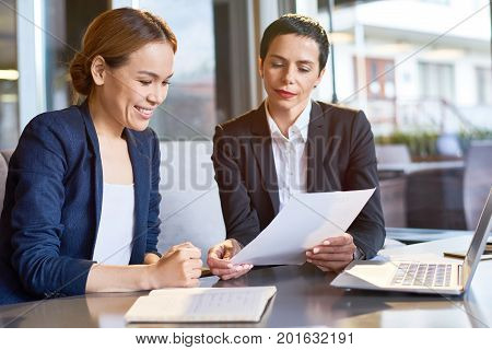 Talented group of financial managers analyzing statistic data while having working meeting in spacious boardroom with panoramic windows