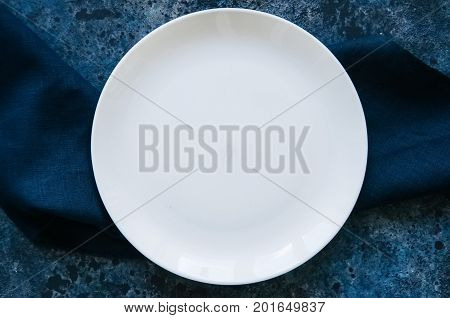 Empty White Round Plate And Linen Blue Sackcloth On A Stone Background.