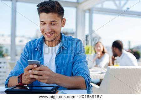 Good news. Low angle shot of a positive minded gentleman in casual looking at a screen of his phone while reading message from his friend outdoors.
