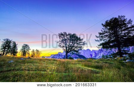 Silhouettes of a man and illuminated tent under a night sky at twilight hour. Alps, Triglav National Park, Slovenia.