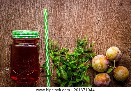 Glass with fresh Plum Juice and green mint on vintage wooden background. Top view. Copy space. Still life. Flat lay