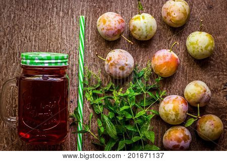 Glass with fresh Plum Juice and green mint on vintage wooden background. Top view. Copy space. Still life. Flat lay