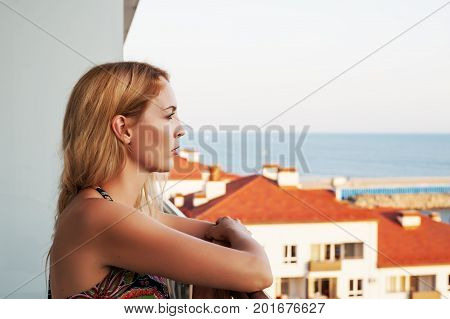 Beautiful woman Looks at the sea from the building's balkon. Visible roofs of neighboring buildings.