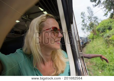 Blonde caucasian woman looking trough old retro blue train window , traveling by train in third world country.