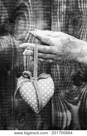 female hand smeared in golden paint or glister holding handmade pink polka dots valentine heart on brown vintage studio background selective focus