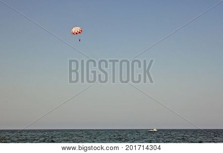 Parachuting over a sea towing by a boat. Paragliding in the clear sky above the sea. Riding on a parachute behind a boat.