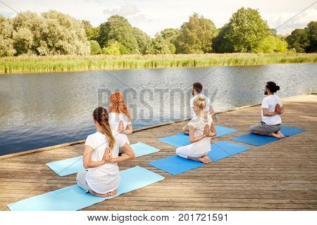 fitness, sport, yoga and healthy lifestyle concept - group of people exercising in reverse prayer pose on river or lake berth
